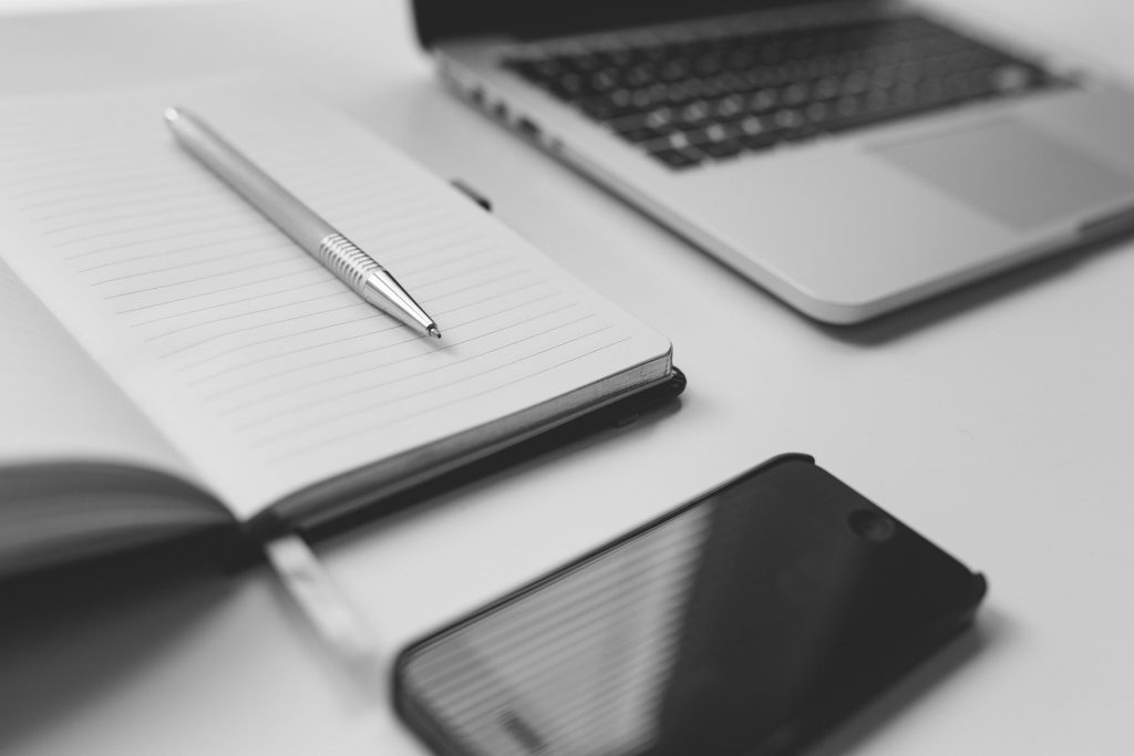 A notebook, cell phone and computer on a desk