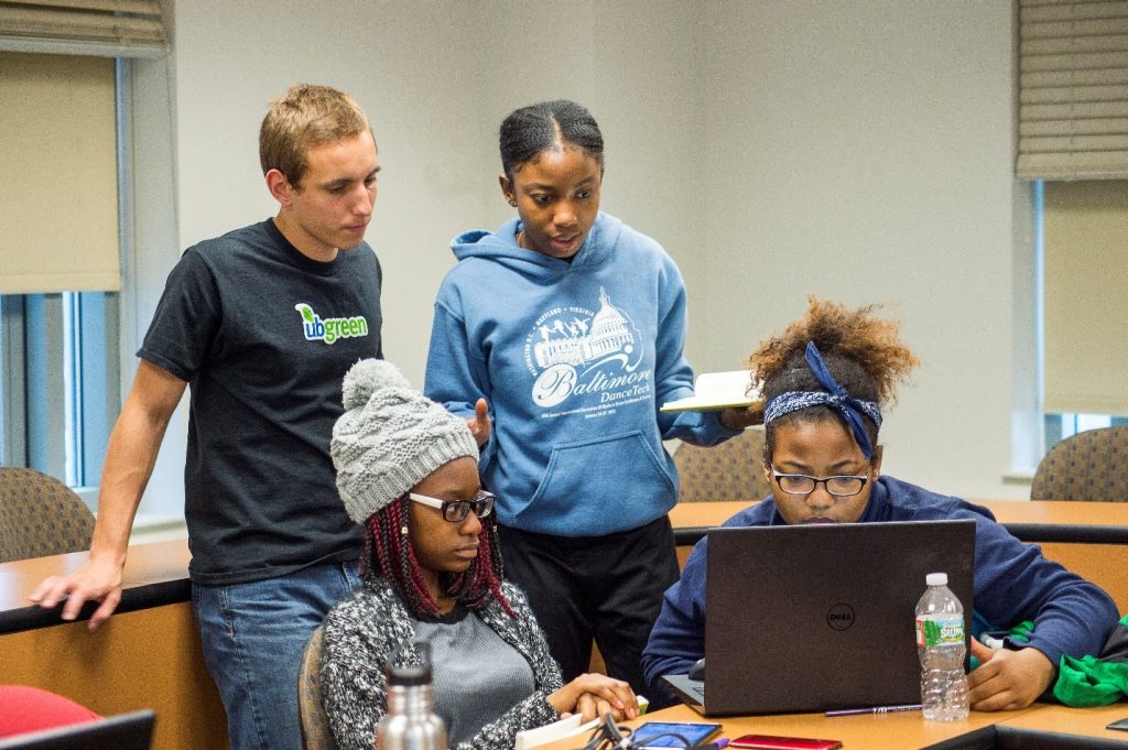 Four UBalt students look at a shared laptop in a classroom