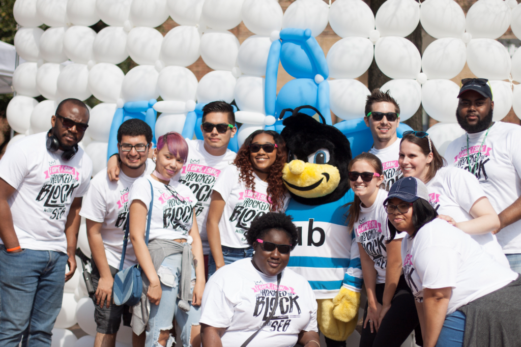 A group of UBalt students pose with the mascot in front of a balloon wall