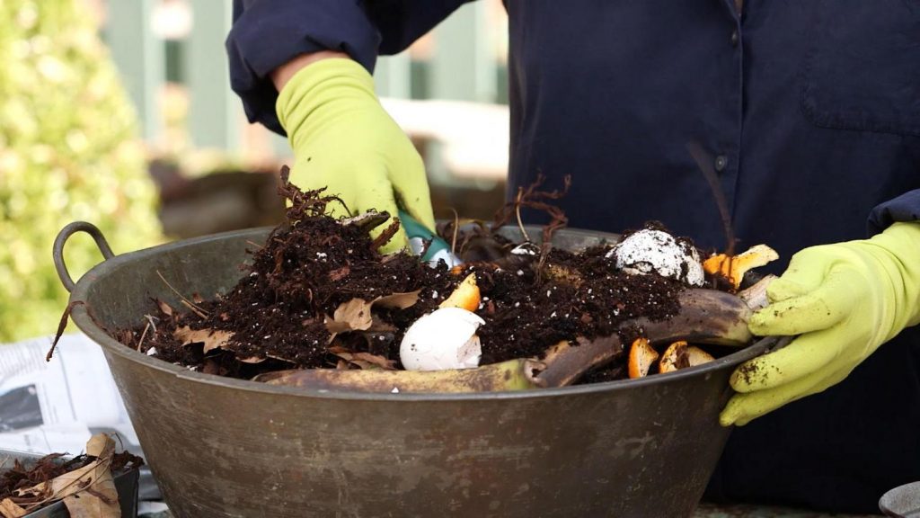 A pair of hands wearing gloves turns compost